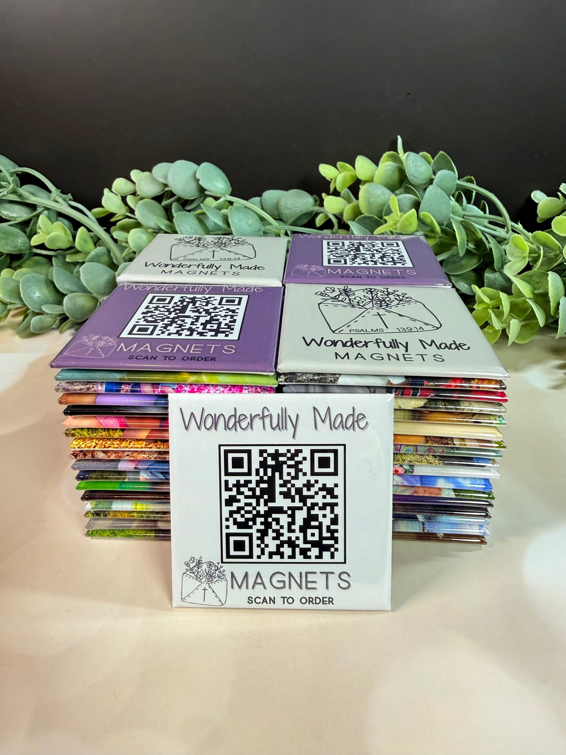 Stack of 2x2 custom photo magnets with assorted images, front magnet featuring website QR code